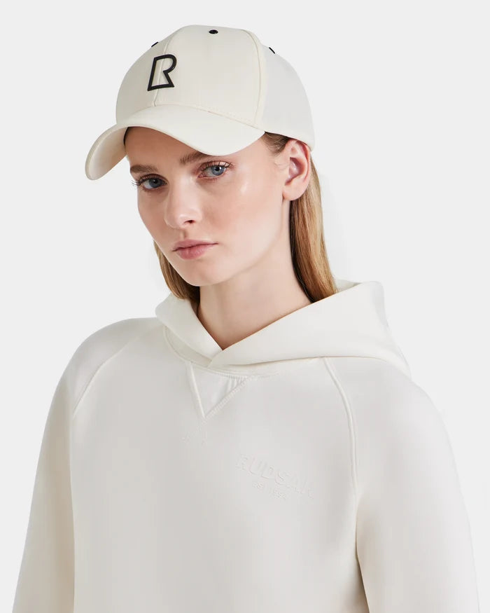 A woman wears the off-white ARSENE - 9422504 Iceland hoodie and a matching unisex Rudsak cap with a black R logo, looking at the camera against a plain light background.