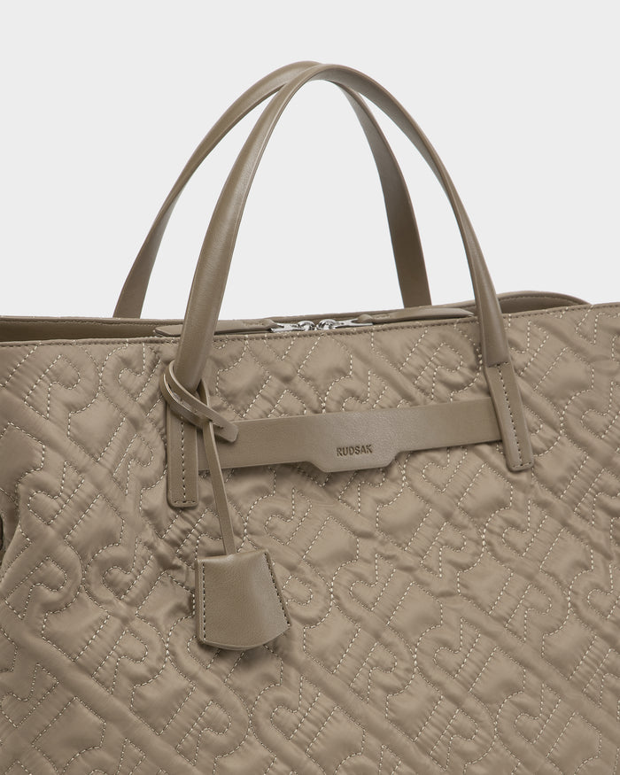 The ASMINE - L325005 Almond by Rudsak is a taupe quilted monogram tote with double handles, embossed pattern, small hanging tag, and a leather accent featuring the Rudsak name—an elegant choice for any occasion.