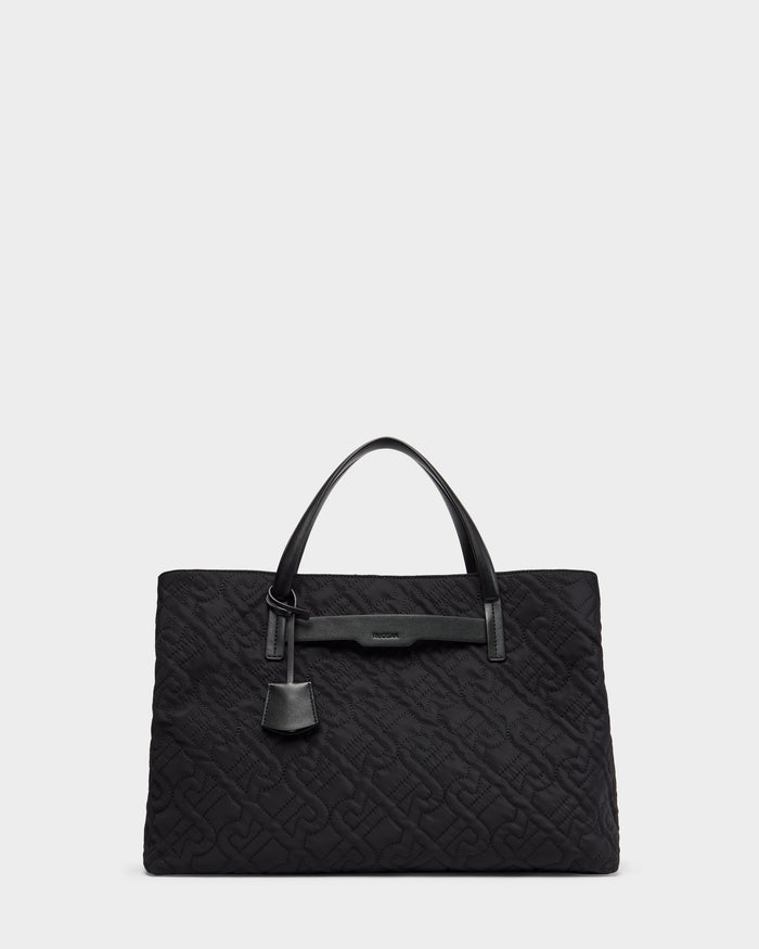 The Rudsak ASMINE - L325005 Black tote features an embossed monogram pattern, two top handles, a leather strap detail, and a hanging leather tag, shown on a plain light grey background.