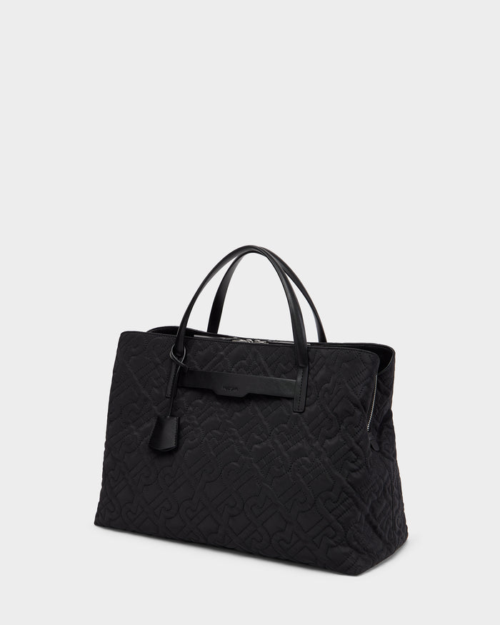 The Rudsak ASMINE - L325005 Black tote features a large quilted design, two leather handles, and a decorative leather tag, shown against a plain light gray background.