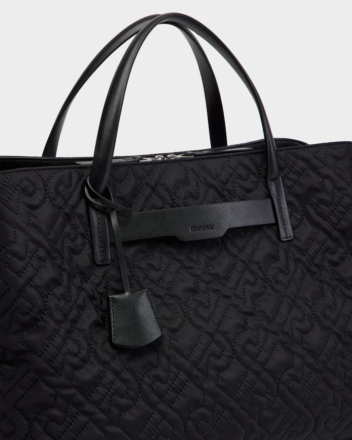 Close-up of the ASMINE - L325005 Black tote by Rudsak, featuring black quilted material, leather handles, a subtle embossed pattern, and a leather tag with the Rudsak name near the top.