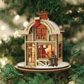 A wooden Christmas tree ornament shaped like a cozy shop, labeled Big Red Sock Stocking Company, hangs on a tree. Warm light glows from inside, and a gingerbread figure stands at the entrance.