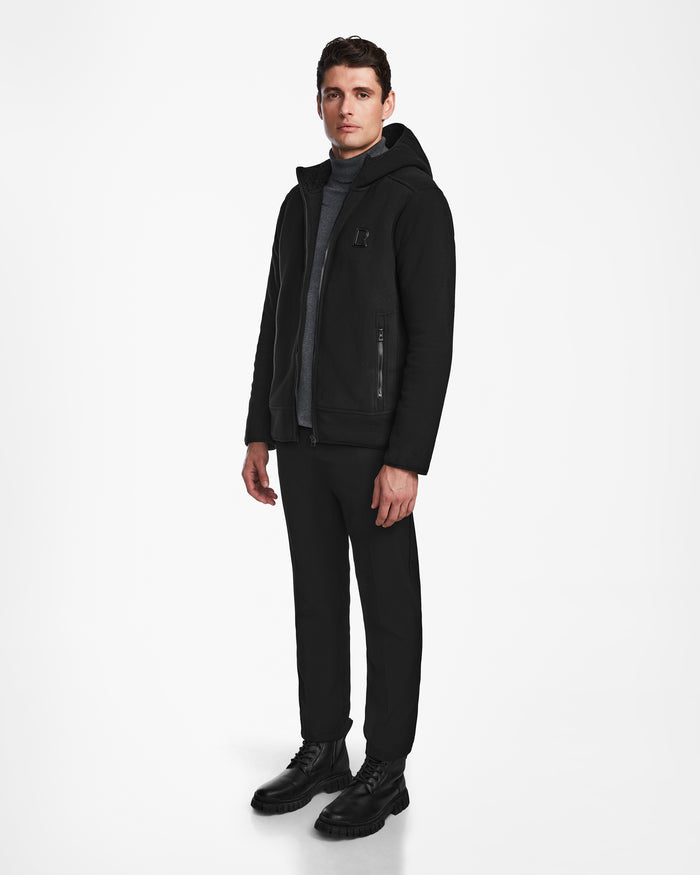 A man wears the Rudsak BILLY - U524501 Black M polar fleece hoodie against a white background, paired with dark pants and lace-up shoes—a stylish, practical winter choice.