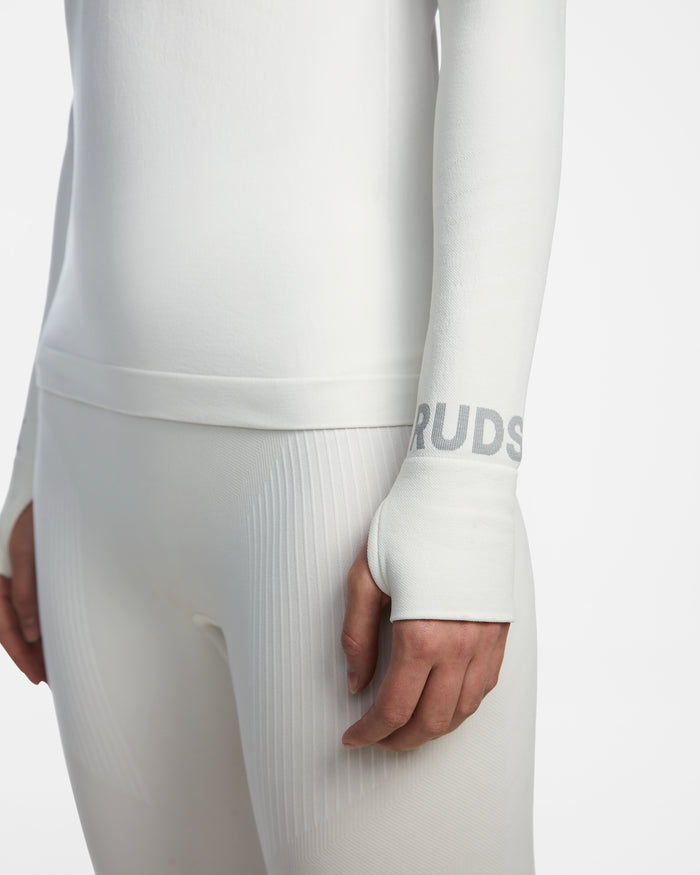 A person wears the Rudsak CARRIE - 8524619 Iceland women’s fitted white thermal set, featuring a long-sleeve ski base layer top with thumb holes, RUDSAK printed on the sleeve, and sleek stretch leggings shown on the lower torso and arm.