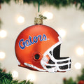 An orange football helmet ornament with the word Gators in blue script hangs on a Christmas tree with blurred lights in the background.