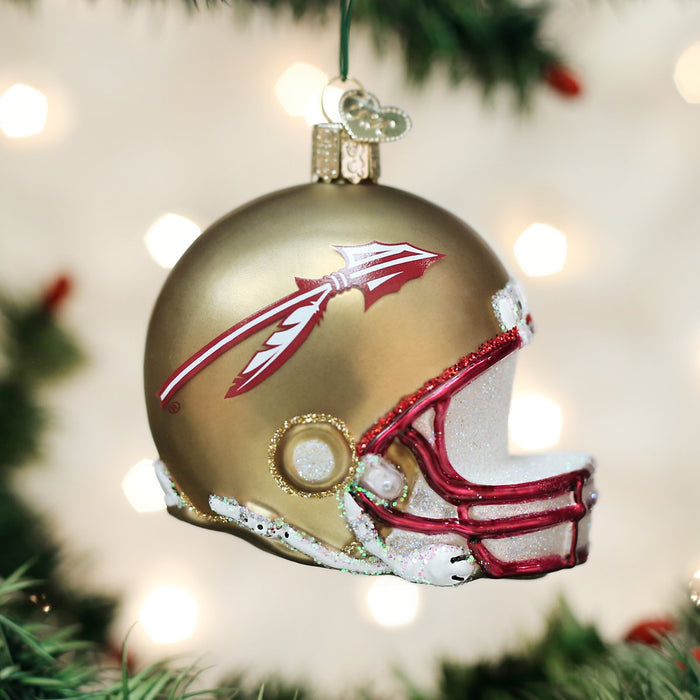 A gold football helmet Christmas ornament with a spear logo and red trim hangs from a tree branch with blurred lights in the background.