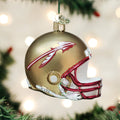 A gold football helmet Christmas ornament with a spear logo and red trim hangs from a tree branch with blurred lights in the background.