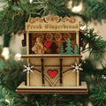 A wooden Christmas ornament shaped like a gingerbread stall hangs on a tree. The sign reads Fresh Gingerbread and features hearts, snowflakes, a gingerbread figure, and a green tree.