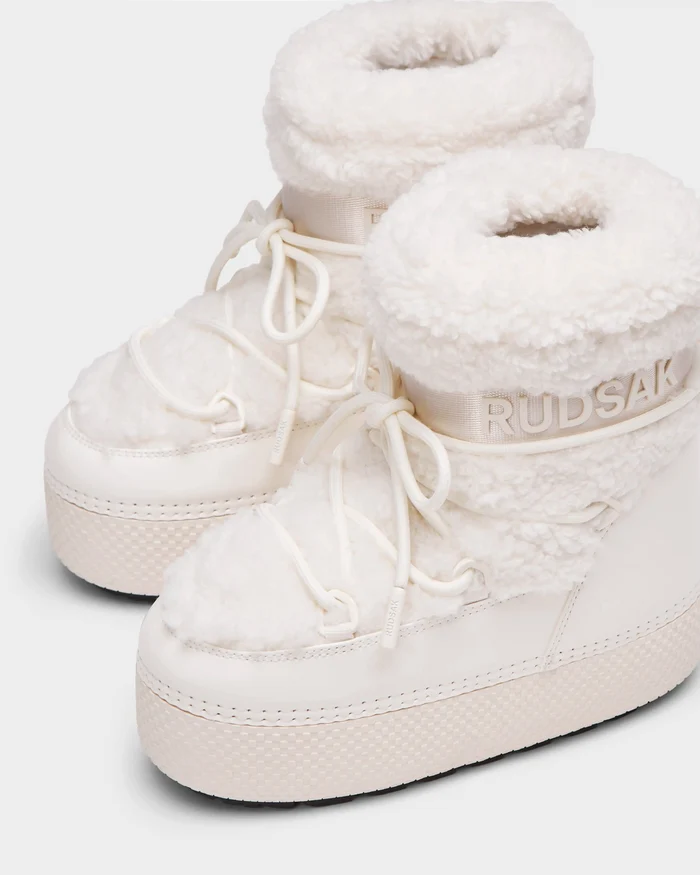 The Rudsak KATHY Y - 1224500 Iceland boots are white, high-top winter boots with thick textured soles, faux fur lining, and laces. Water-repellent and insulated, they feature the Rudsak logo on the side for a cozy, stylish look.