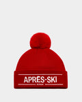 The KRISS - 9424500 Flame Red by Rudsak is a bold unisex ski tuque with a large pom-pom and cuff embroidered in white with APRÈS-SKI above RUDSAK. This classic après-ski essential pops against a plain white background.