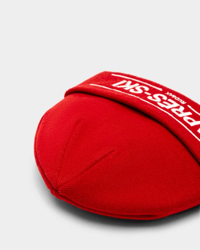 A close-up of the KRISS - 9424500 Flame Red by Rudsak, a red fabric-covered protective pad with a PRESS-SIN strap in white text—ideal for après-ski storage next to your merino wool hat, set against a light gray background.