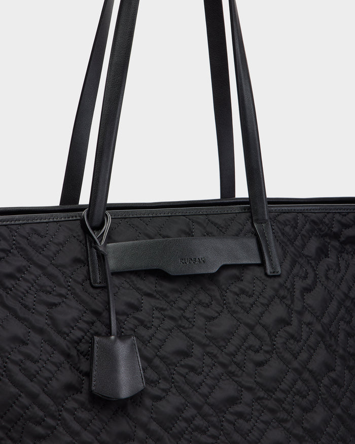 Close-up of the Rudsak LIVORNO - L325007 Black quilted tote bag, featuring embossed patterns, two shoulder straps, a small leather tag, and a subtle embossed Rudsak logo near the top.