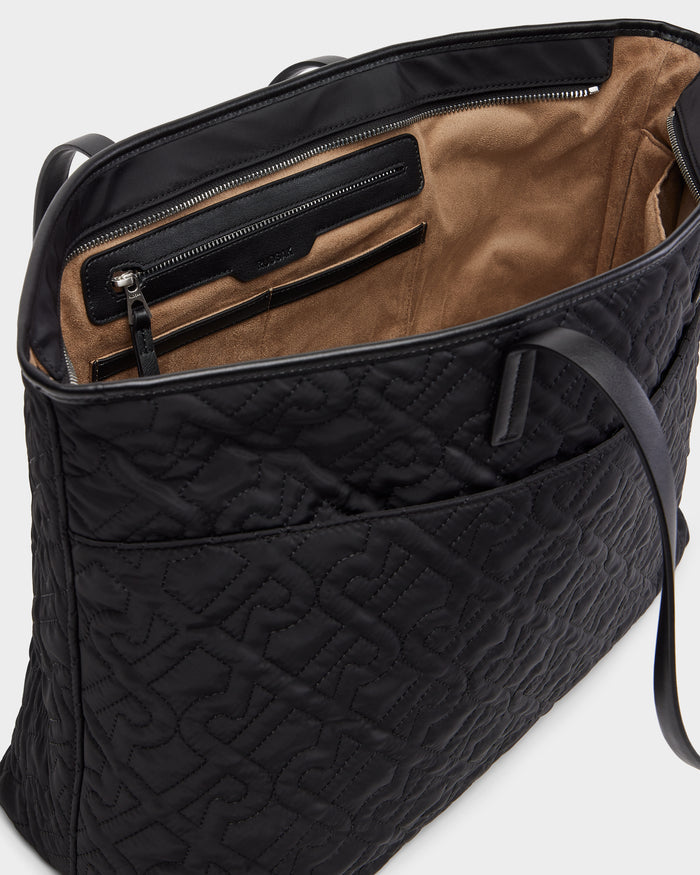 A close-up of the Rudsak LIVORNO - L325007 Black tote bag shows its black quilted exterior and brown suede interior, complete with an inner zippered pocket and card slots.