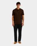 A man faces forward, modeling the Rudsak MAISEN - 6524518 Mocha short-sleeve polo shirt with black pants and brown shoes against a plain light gray background.
