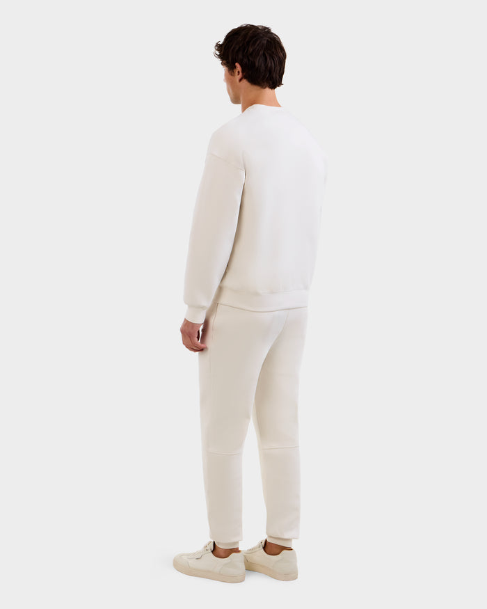 A man faces away from the camera, wearing the Rudsak MAXTON - U525007 Vanilla M cotton-blend jogger and sweatshirt set with sneakers, set against a plain white background.