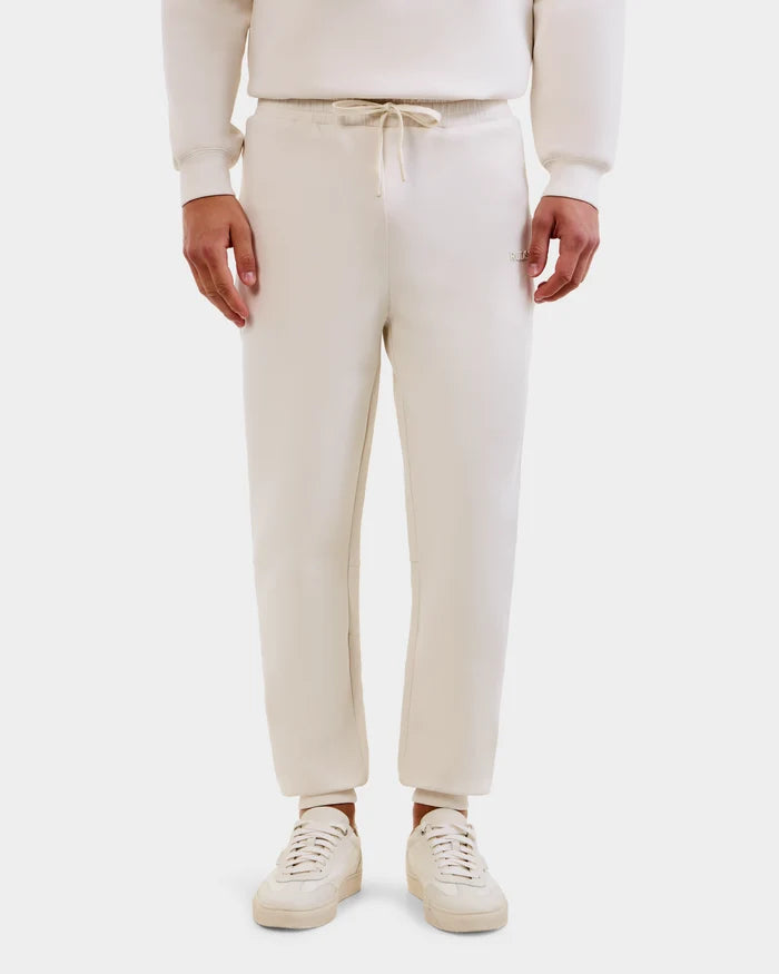 A person wearing Rudsak MAXTON - U525007 Vanilla M jogger sweatpants stands against a white background. Only the lower half is visible, showcasing the relaxed fit and everyday comfort of these unisex pants.