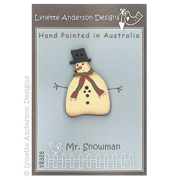 A hand painted wooden button in the shape of a snowman with a hat, scarf, and a grinning face, packaged on a card with the artist's signature.