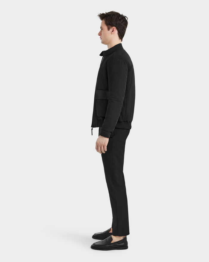 A man stands in profile facing left, wearing the Rudsak PETER - 6125001 Black jacket with vegan leather accents, paired with black pants and black shoes against a plain white background.