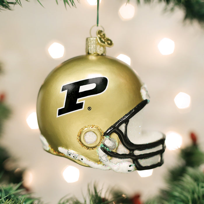 A gold football helmet Christmas ornament with a black P logo, hanging from a tree with green branches and white lights blurred in the background.
