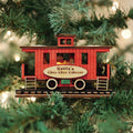 A red wooden train caboose ornament labeled Santas Choo Choo Caboose hangs on a Christmas tree, surrounded by green branches and twinkling white lights.