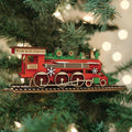 A wooden â€œNorth Pole Expressâ€_x009d_ train ornament, painted red and green with snowflake decorations, hangs on a Christmas tree with blurred white lights in the background.