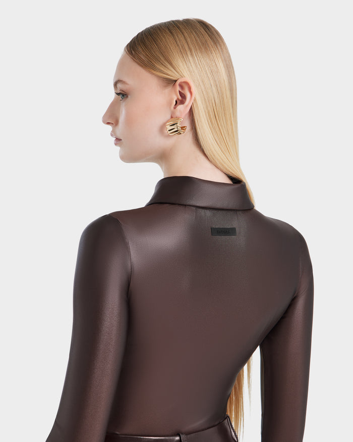 A woman with long, straight blonde hair models the Rudsak SHELLY - 8524537 bodysuit in espresso, styled with gold statement earrings. She is photographed from the back and in profile against a plain white background.
